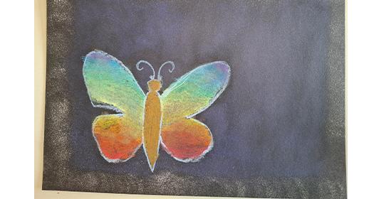  Das Bild zeigt die Kreidezeichnung eines Schmetterlings auf einem dunklen Untergrund. Die Flügel des Schmetterlings sind in einem Regenbogenfarbverlauf von Blau über Grün nach Gelb und Orange bis Rot schattiert. Der Körper des Schmetterlings ist in einem hellen Gelbton gezeichnet.